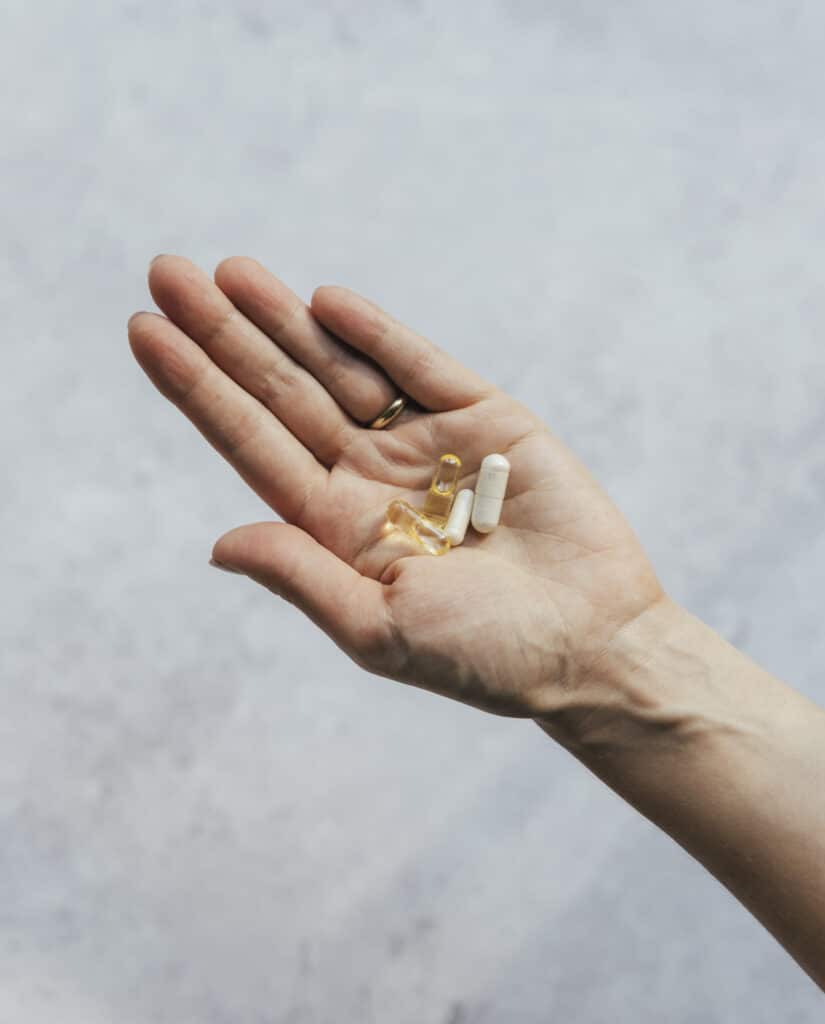 Mão de mulher aberta com 4 cápsilas de suplementos sobre um fundo cinzento azulado